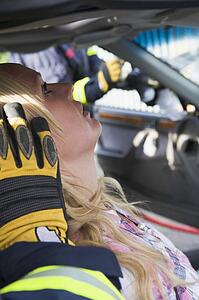 Injured woman in car with firefighter in background cutting out windshield (selective focus)