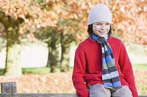 Young boy outdoors at park sitting on fence smiling (selective focus)