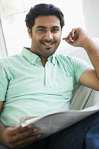 Man in living room with newspaper smiling (high key/selective focus)