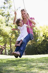 Woman and young girl outdoors on tree swing smiling
