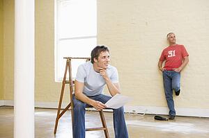 Two men with ladder in empty space one holding paper smiling