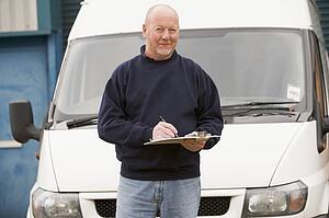 Deliveryperson standing with van writing in clipboard