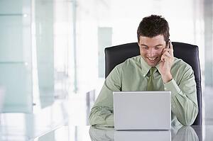 Businessman sitting in office using cellular phone and laptop