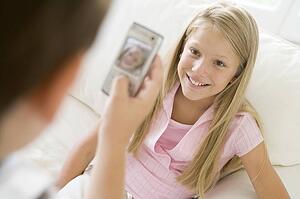 Young boy taking picture of smiling young girl with camera phone indoors
