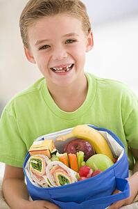 Young boy holding packed lunch in living room smiling