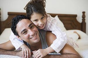 Man and young girl relaxing on bed in bedroom smiling (selective focus)