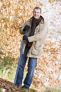 Man outdoors raking leaves and smiling (selective focus)