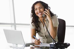 Businesswoman in office on telephone by laptop smiling (high key/selective focus)