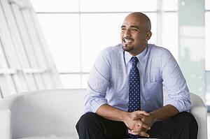 Businessman sitting indoors smiling (high key/selective focus)