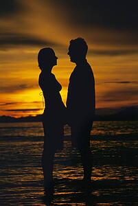 Couple standing on the beach holding hands at sunset (silhouette)