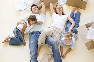 Family lying on floor by open boxes in new home smiling