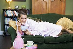 Young woman lying on sofa at home eating a sweet treat