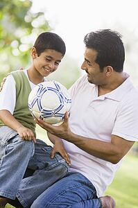 Father and son outdoors in park with ball smiling (selective focus)