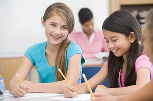 Students in class writing with teacher in background (selective focus)
