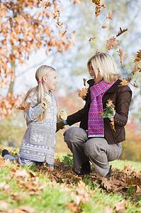 Woman and young girl outdoors in park playing in leaves and smiling (selective focus)