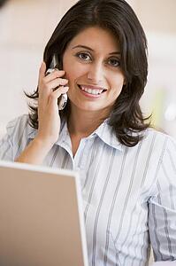 Woman in kitchen with laptop and cellular phone smiling