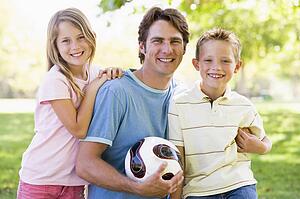 Man and two young children outdoors holding volleyball and smiling