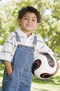 Young boy holding soccer ball outdoors smiling