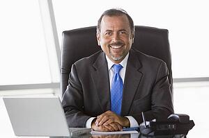 Businessman in office with laptop smiling (high key/selective focus)