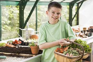 Young boy in greenhouse holding basket of vegetables smiling