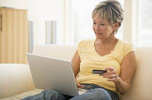 Woman in living room with laptop and credit card smiling