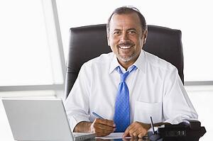 Businessman in office with laptop smiling (high key/selective focus)
