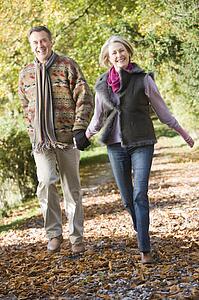 Couple outdoors running on path in park holding hands and smiling (selective focus)