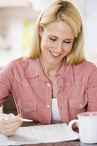 Woman in kitchen with newspaper and coffee smiling