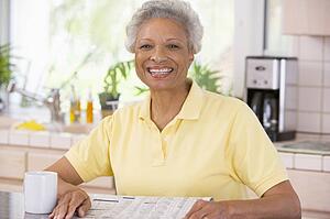 Woman relaxing with newspaper in kitchen and smiling