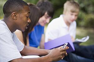 Four students outdoors studying with one checking cellular phone (depth of field)