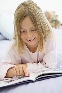 Young Girl Lying On Her Bed In Her Pajamas, Reading A Book