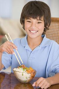Young boy in dining room eating chinese food smiling