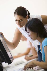 Two women in computer room where one is assisting the other