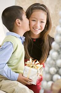 Brother Kissing His Sister On The Cheek, And Holding A Christmas Gift