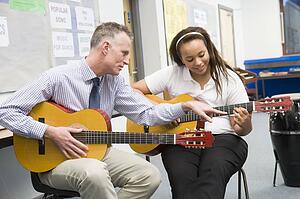 Female student receiving guitar lesson from teacher in classroom