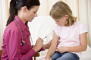 Doctor giving needle to young girl in exam room