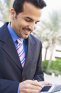 Businessman outdoors using personal digital assistant and smiling (high key/selective focus)
