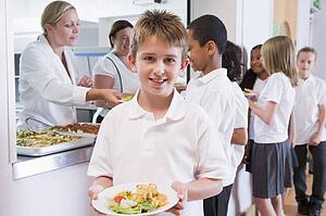 Students in cafeteria line with one holding his healthy meal and looking at camera (depth of field)