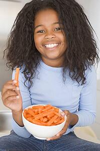 Young girl in kitchen eating carrot sticks smiling