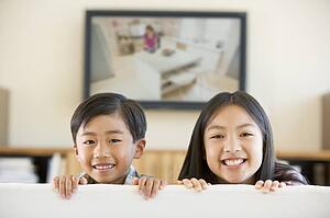 Two young children in living room with flat screen television smiling