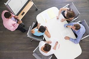Four businesspeople at boardroom table watching presentation