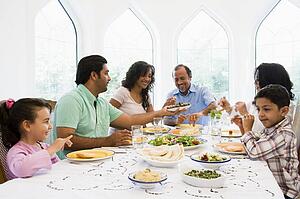 Family sitting at dinner table smiling (high key)