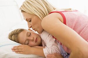 Woman waking young girl in bed with a kiss