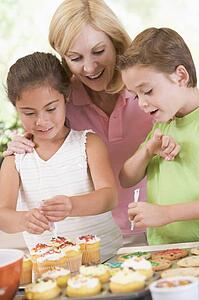 Woman with two children in kitchen decorating cookies smiling