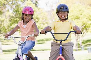 Brother and sister outdoors on bicycles smiling