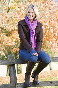 Woman outdoors sitting on fence smiling (selective focus)