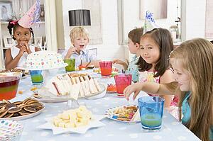 Young children at party sitting at table with food smiling