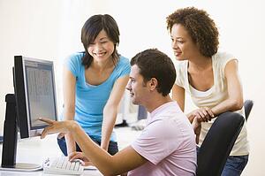 Three people in computer room pointing at monitor and smiling
