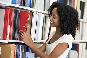 Woman in library pulling book off a shelf (depth of field)