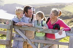 Family on cliffside path leaning on fence and smiling